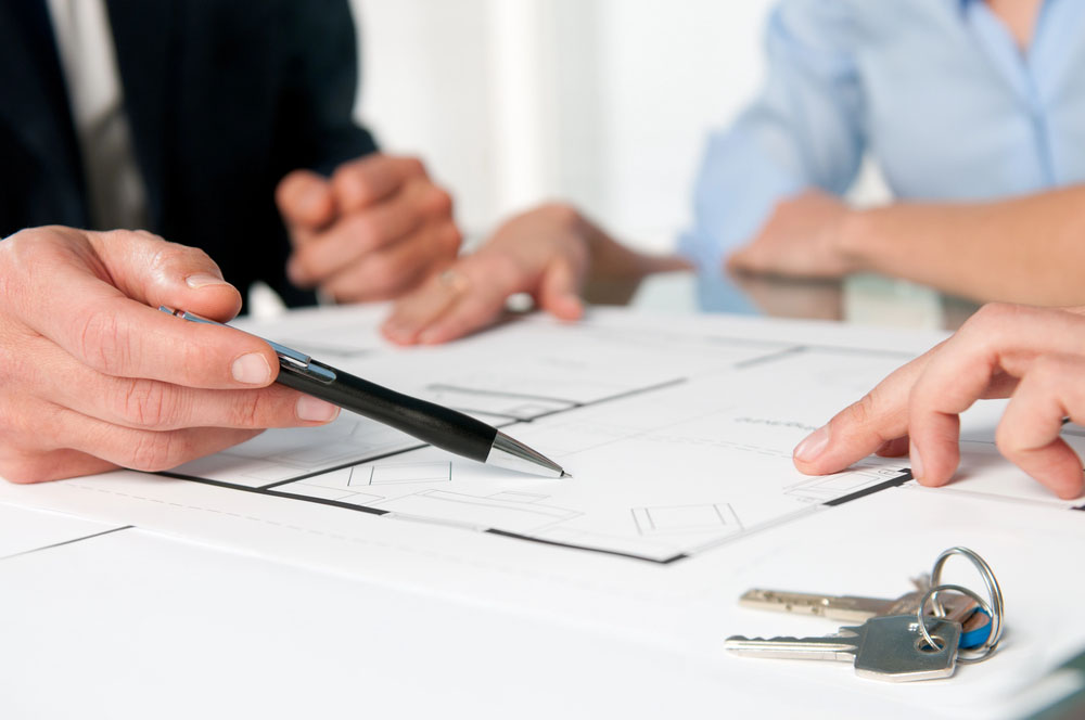Closeup view of new home keys and house plan during a discussion with a real estate agent